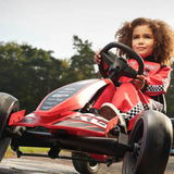 Child in a red go-kart on a track with trees in the background