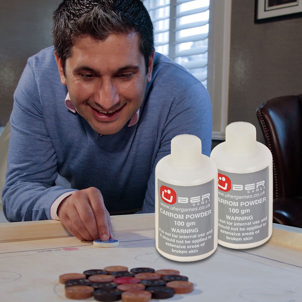 an playing carrom while smiling, with two Uber Games carrom powder 100g bottles positioned in the foreground