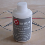 Uber Games carrom powder 100g bottle placed on a carrom board, featuring the board's centre star design in the background