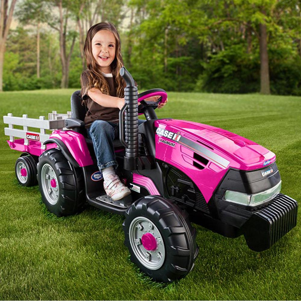 Child sitting in a pink toy tractor with a white trailer on grass