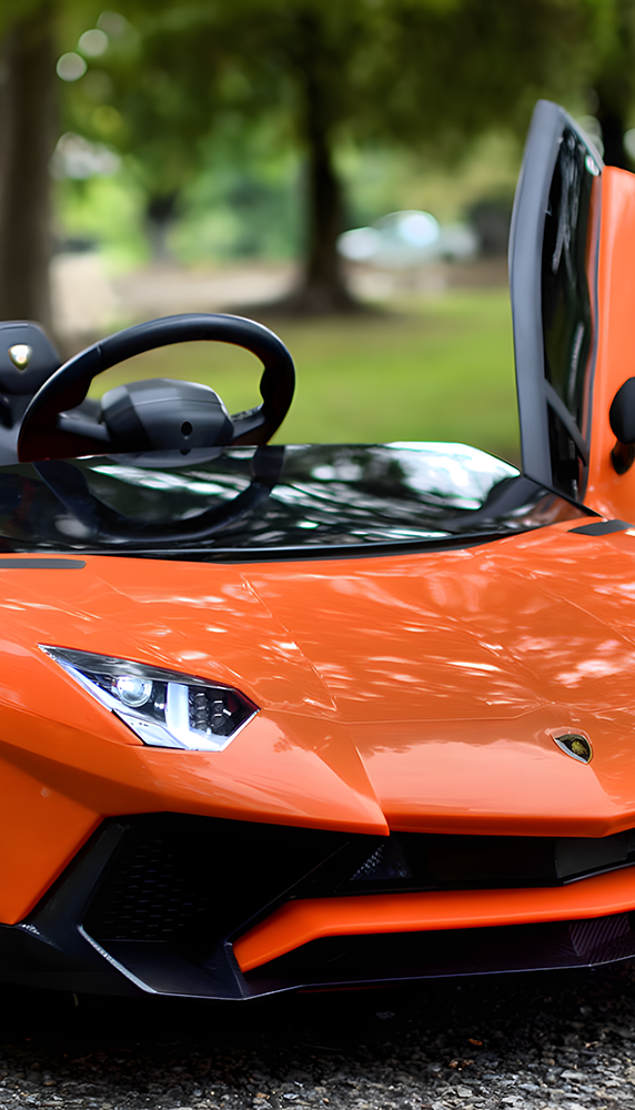 Close-up of the front of an orange sports car, showcasing its sleek headlights and aerodynamic design.