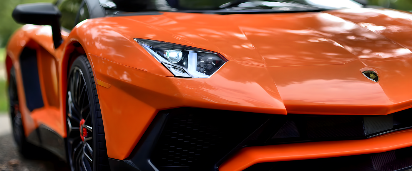 Close-up of the front of an orange sports car, showcasing its sleek headlights and aggressive design lines