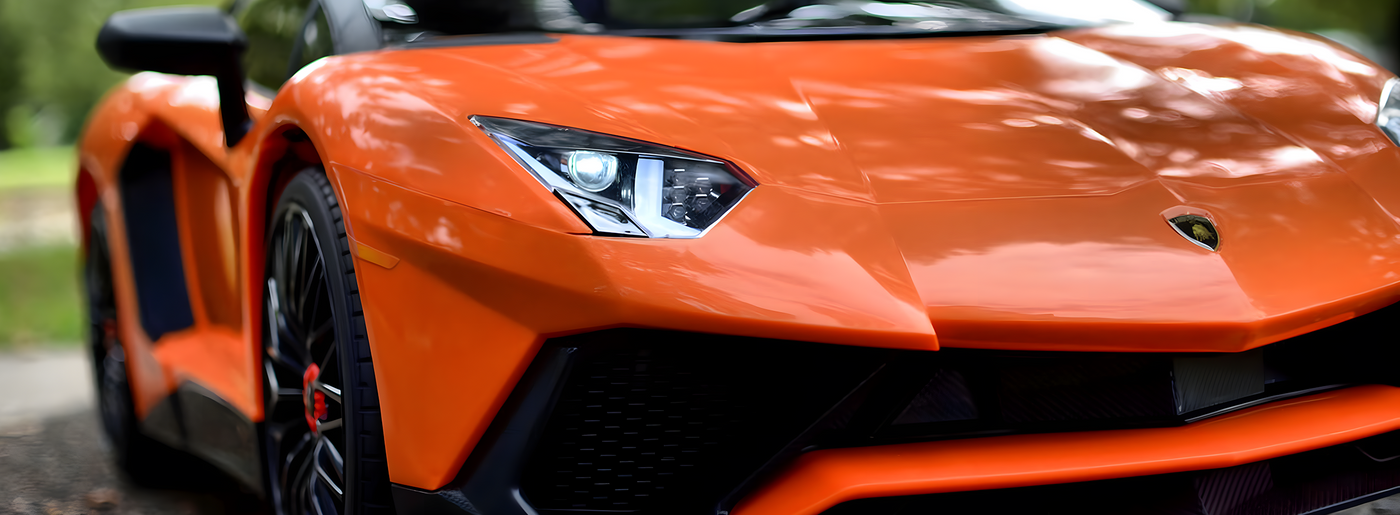 Close-up of the front of an orange sports car, showcasing its sleek headlights and aerodynamic design.