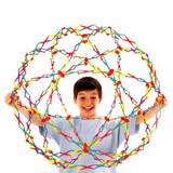 Young boy holding a large, multi-coloured Hoberman Sphere in its expanded form, smiling against a white background