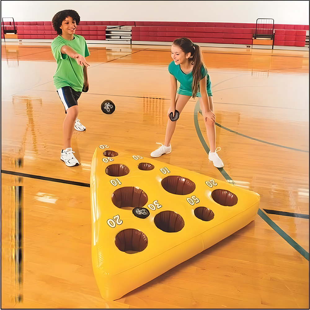 Children playing the Mouse and Cheese Toss game in a gym, trying to throw beanbags into holes on a yellow inflatable cheese mat