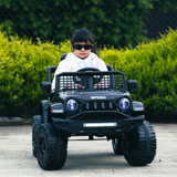 A young girl wearing sunglasses, driving the black Jeep-inspired remote-controlled ride-on electric car, with greenery in the background.