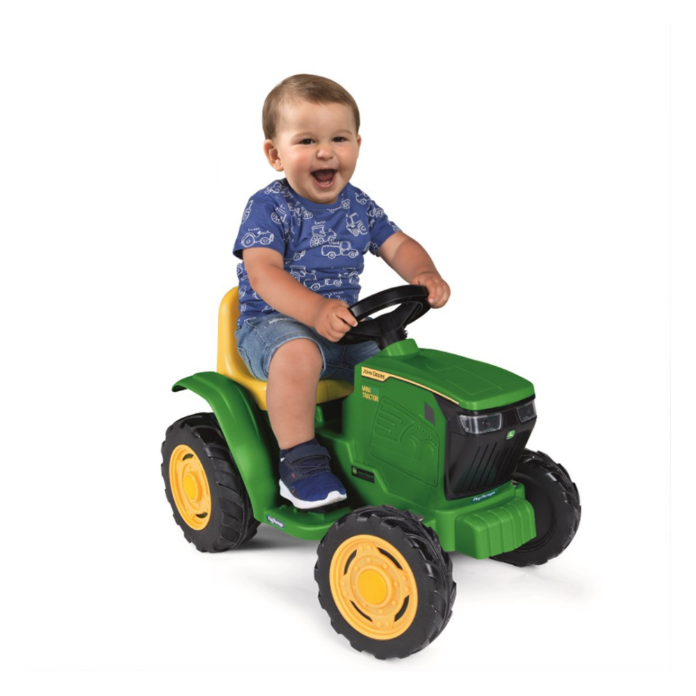 Child sitting on a green toy tractor with a white background