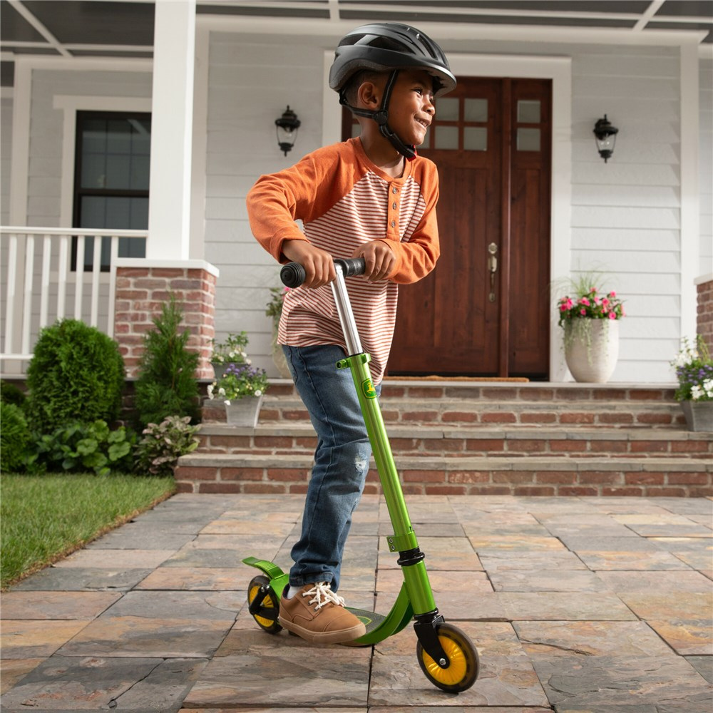Child riding a green scooter in front of a house