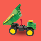 A green and yellow John Deere toy dump truck with its bed raised, shown on a solid red background. A red arrow graphic points upward near the bed to indicate lifting.