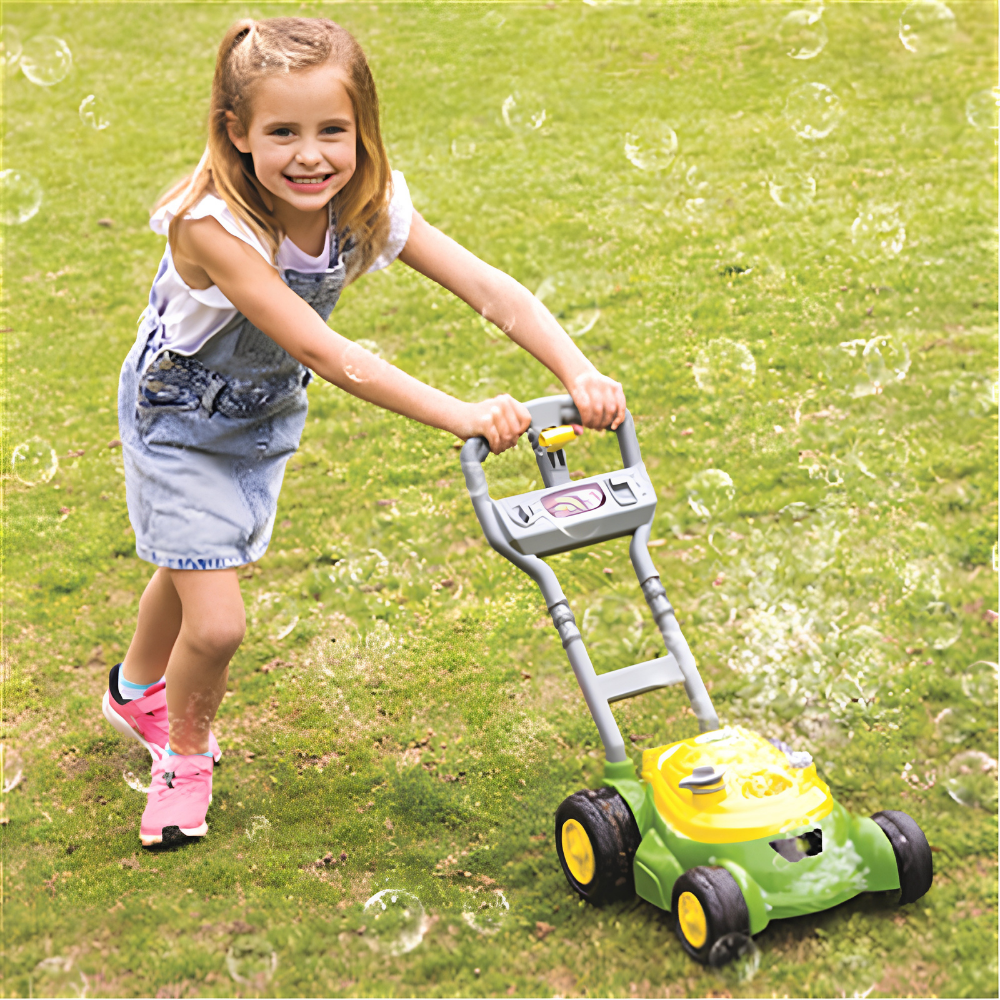 A young girl pushing a green and yellow toy lawn mower with a gray handle on a grassy lawn, surrounded by floating bubbles.