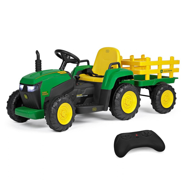A green and black John Deere-style ride-on toy tractor with a yellow seat and yellow plow attachment, shown on a white background with a black remote control in front.