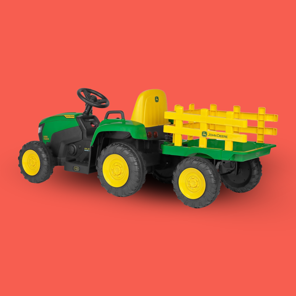 A John Deere toy ride-on tractor with a green and yellow body, black tires, and a matching green and yellow pull-on trailer, shown on a solid coral-red background.