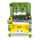 A John Deere toy repair station playset with a green and gray workbench, yellow storage bin, hanging tools, and a green toy tractor on a white background.