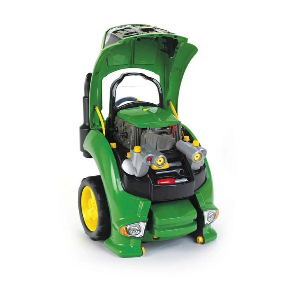 A green toy tractor with its hood open, revealing a detailed toy engine with gray components, yellow knobs, and small red accents, set against a plain white background.