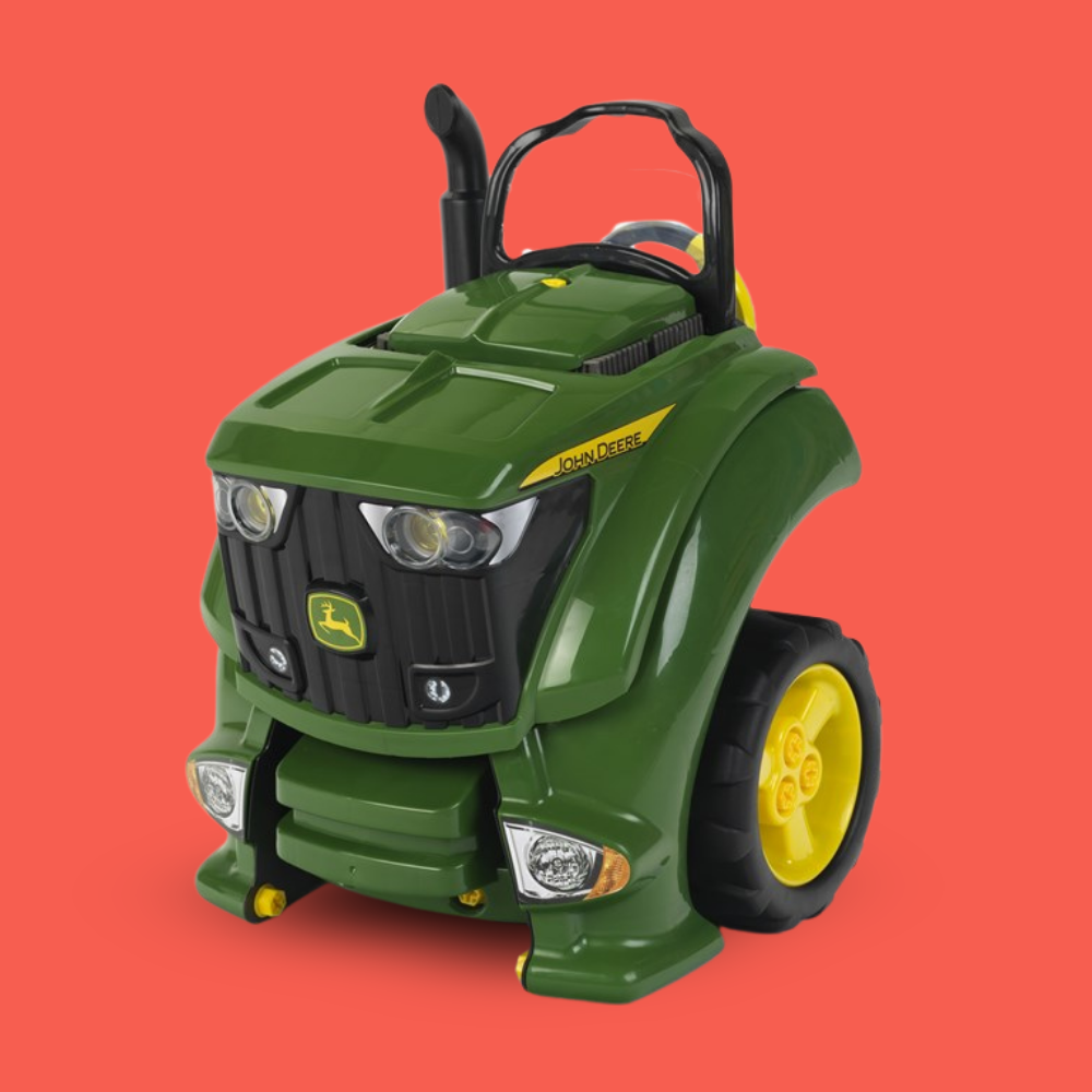 A green John Deere ride-on toy tractor with black wheels and yellow accents, shown on a solid coral-red background.