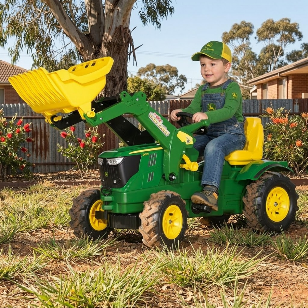 Child playing with a green toy tractor with yellow attachments in a backyard setting.