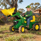 Child playing with a green toy tractor with yellow attachments in a backyard setting.