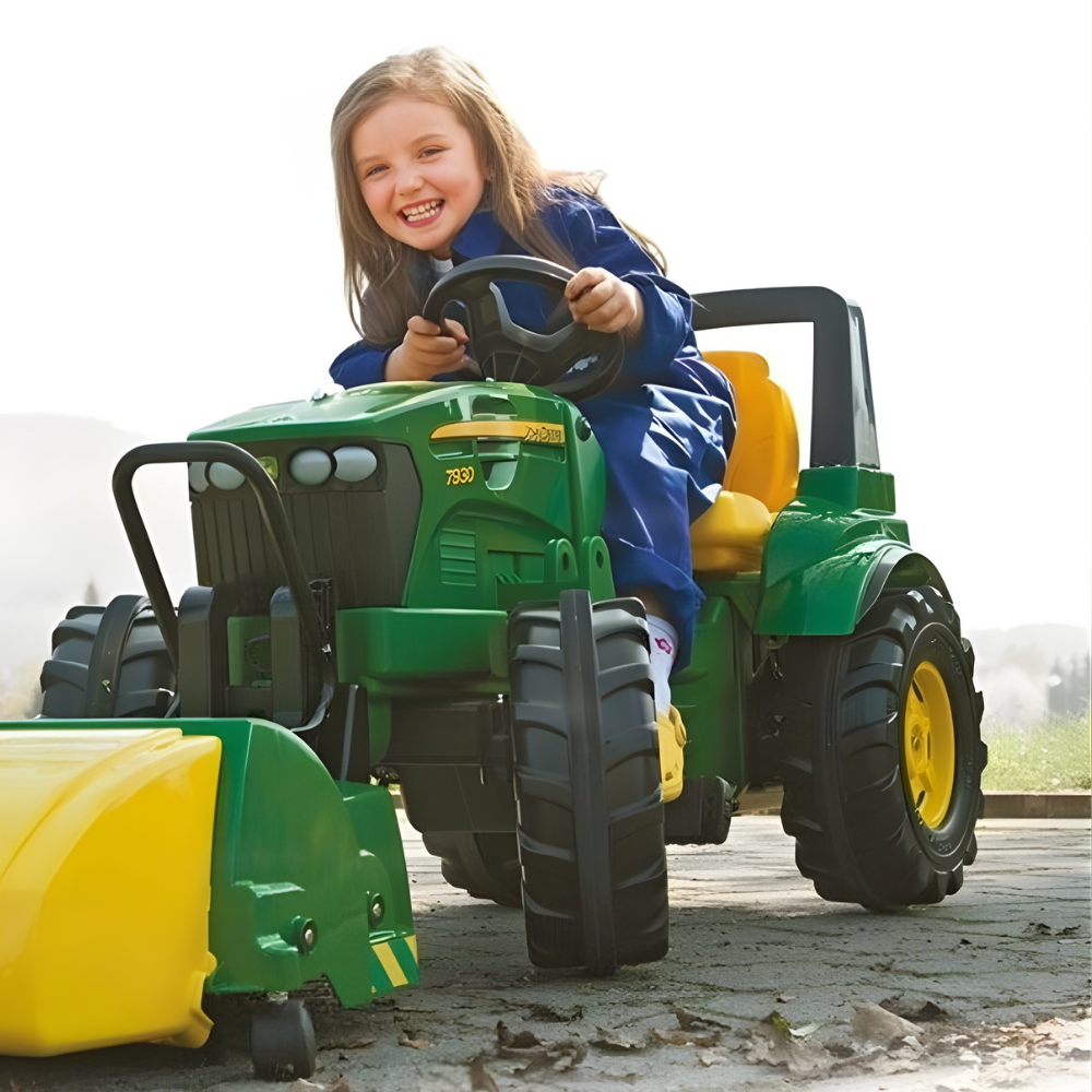 Child playing with a green toy tractor on a paved surface.
