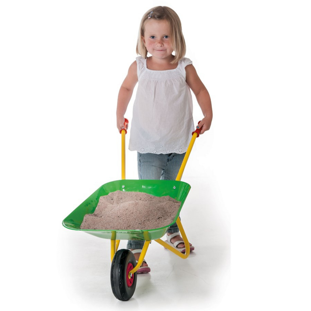 Child pushing a green wheelbarrow filled with sand on a white background