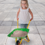 Child pushing a green wheelbarrow filled with sand on a tiled floor