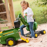 Child playing with a green toy tractor in a sandy area