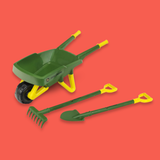 A toy garden tool set including a green and yellow wheelbarrow, a green rake, and a green and yellow shovel, displayed on a solid coral-red background.