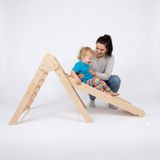 Child playing on a wooden climbing toy with a woman on a white background