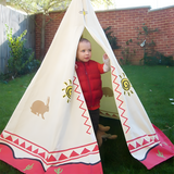 Toddler standing inside a cream-coloured wigwam teepee with desert-themed designs, set up in a backyard with a grass lawn