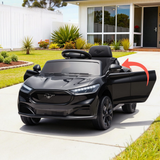 A black Ford Mustang-themed kids' ride-on toy car parked on a concrete driveway in front of a modern house. The toy car has a glossy black finish, black wheels, and a black steering wheel.