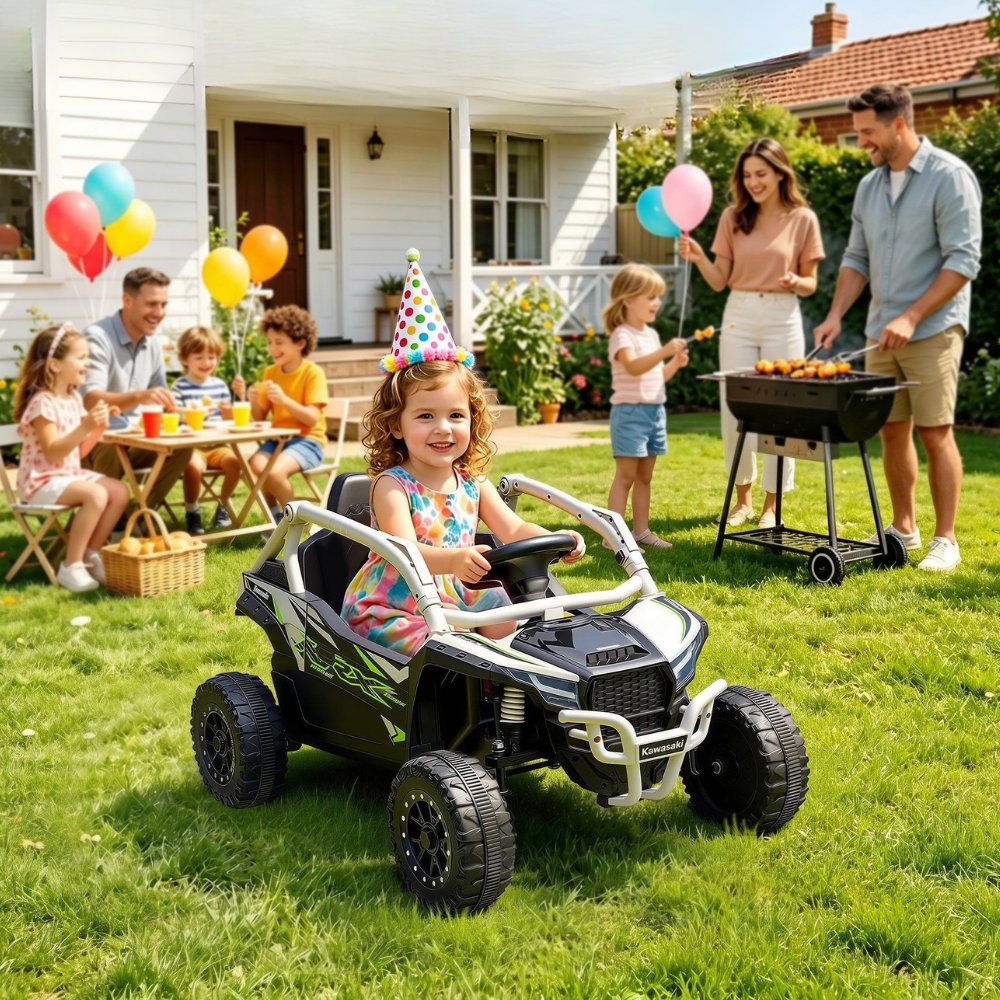 A young girl wearing a party hat drives a black and silver ride-on ATV on a green grassy backyard. In the background, a family is gathered around a barbecue grill and a table with balloons, celebrating a birthday.