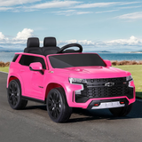 Pink Chevrolet Tahoe-inspired ride-on electric car for kids, parked on a road with a scenic background of mountains and water.