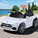 White toy car with Mercedes-Benz logo on a paved area near a house and lake.