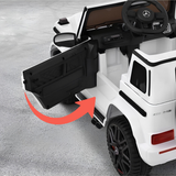 White children's ride-on vehicle styled like a Mercedes-Benz G-Class, showing the open front door with a red arrow indicating the swing motion. The vehicle has black wheels, a black steering wheel with a Mercedes-Benz logo, and a gray concrete floor background.