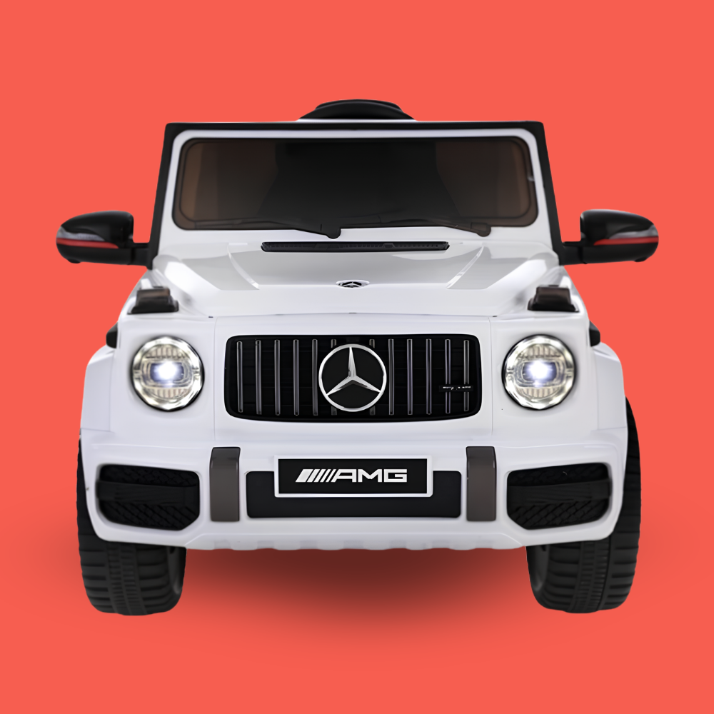 A white Mercedes-Benz G-Class style ride-on toy car shown from the front against a solid coral-red background. The front grille features the Mercedes-Benz logo, with 'AMG' branding on the bumper and side mirrors.
