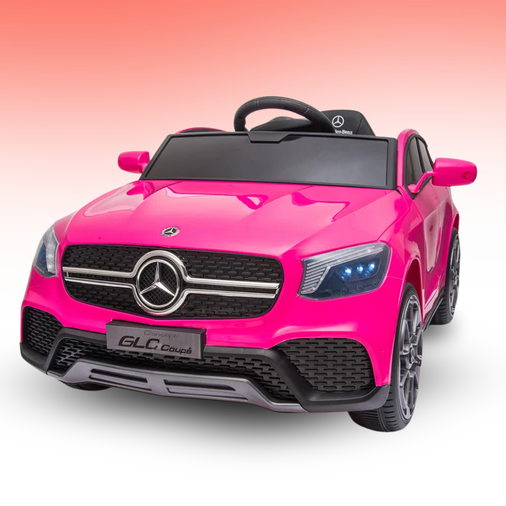 A bright pink Mercedes-Benz GLC Coupe ride-on toy car with a black steering wheel, black grille, and gray wheels, shown on a white background with a pink gradient sky.