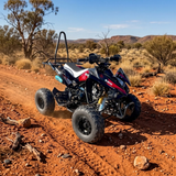 A red, white, and blue mini ATV with a black roll bar is shown driving on a red dirt road in a desert landscape.