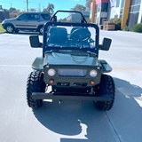 Green off-road vehicle on a paved surface with buildings in the background