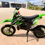 Green and black dirt bike on a concrete surface with buildings and cars in the background