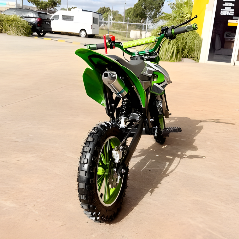 Green dirt bike parked on a concrete surface with vehicles and trees in the background