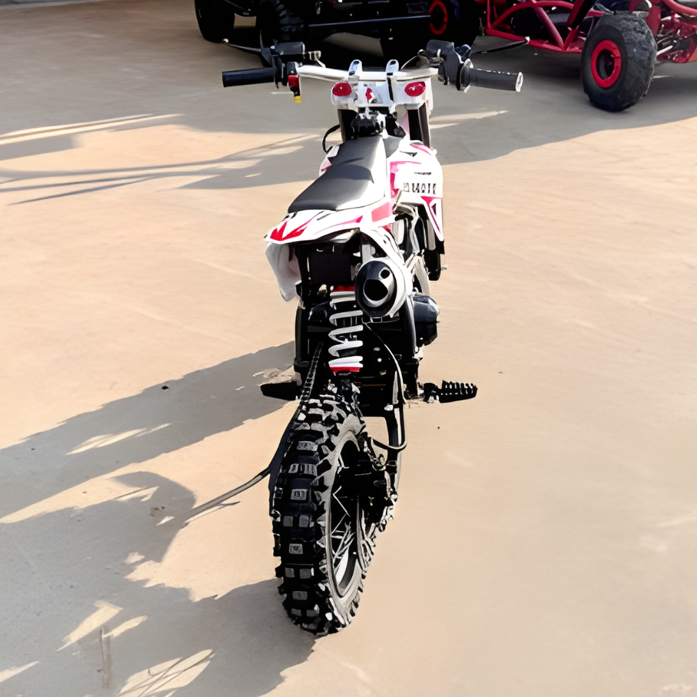 Small dirt bike on a sandy surface with a larger vehicle in the background.
