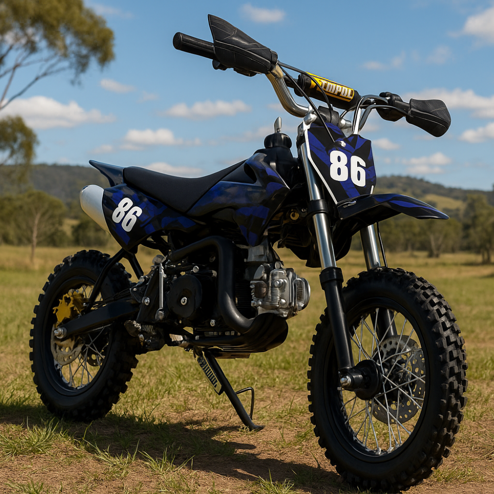 Outdoor shot of blue and black dirt bike on dirt terrain with trees in the background, positioned front-left to show tread and stance.