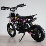 Rear-angled studio shot of the dirt bike, focusing on rear tyre, chain, and exhaust.