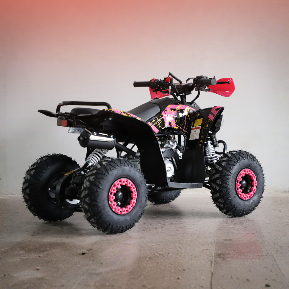 A black mini ATV quad bike with pink and white graphic decals, black knobby tires, and bright pink wheel rims, parked on a concrete floor against a gray wall.