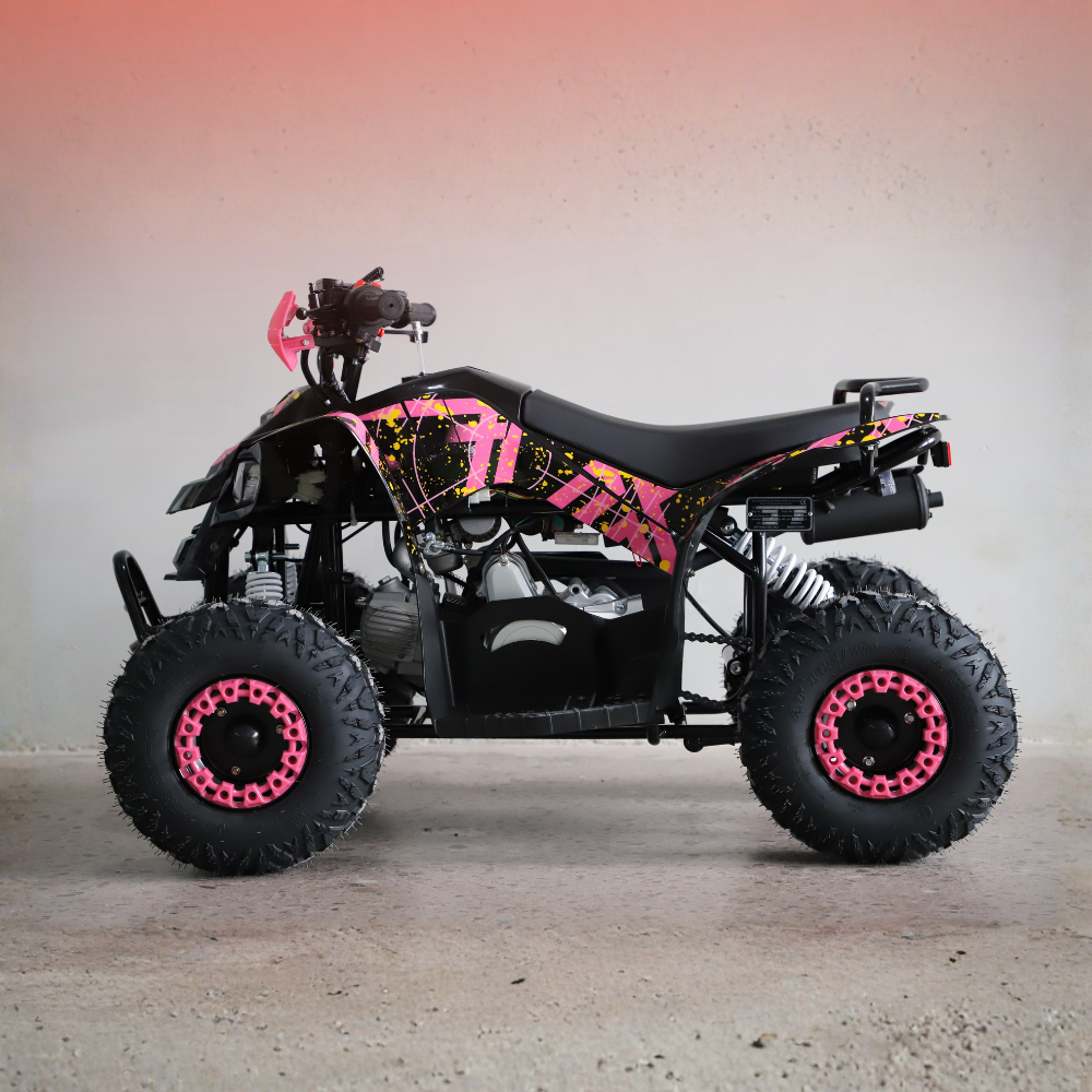 A small black ATV with bright pink and yellow graphic decals, parked against a plain light gray wall with a warm pinkish glow near the top.
