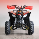 A black and red ATV with large knobby tires, red handlebar grips, and a front protective bumper, photographed against a plain light gray wall.