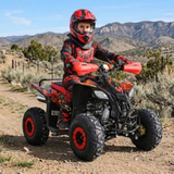 A child wearing a red and black motocross helmet and matching red and black riding suit sits on a red and black quad bike ATV on a dirt path with mountains in the background.