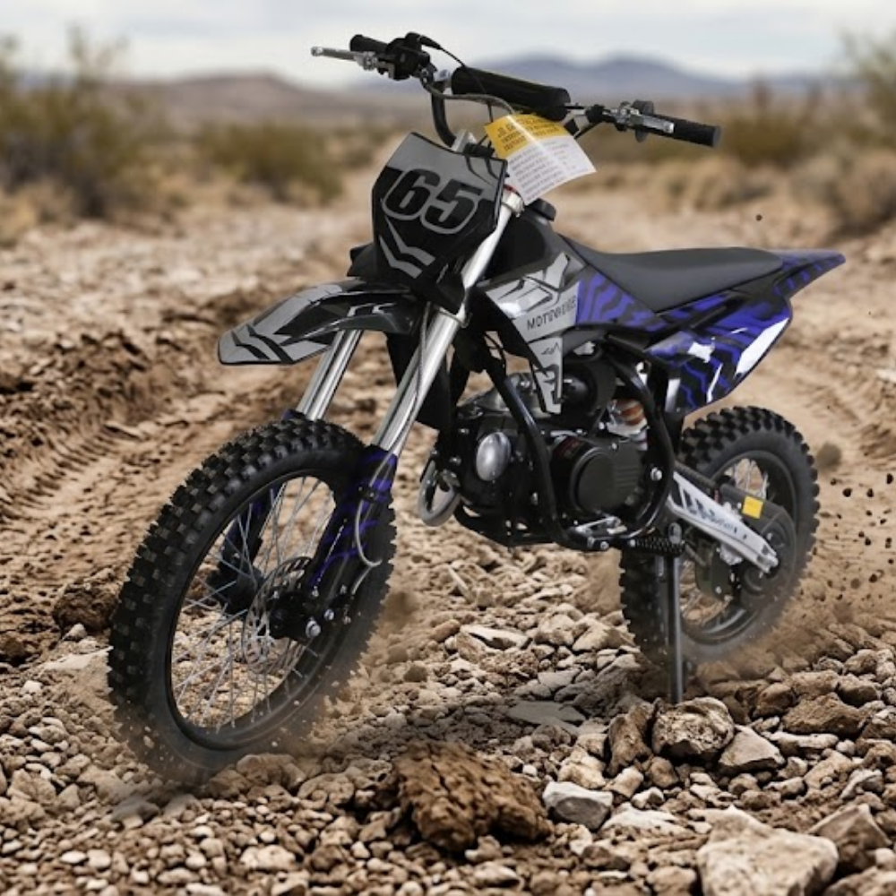 A youth dirt bike with a black, white, and blue color scheme, featuring the number 65 on the front fender, shown riding on a rocky dirt track in a desert landscape.