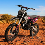 A pink and black dirt bike with the number 65 on its front plate, parked on a red dirt road with a blurred outdoor desert background.