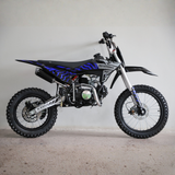 A silver and black mini dirt bike with blue graphic decals, photographed from a side profile against a plain light gray wall.