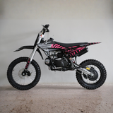 A mini dirt bike with a black and pink zebra-stripe pattern, photographed from the side against a plain light gray wall and concrete floor.